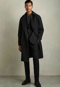 Palton negru cu un design cu două rânduri de nasturi, asortat cu un pulover închis la culoare și pantaloni eleganți. Material fin și siluetă ajustată.