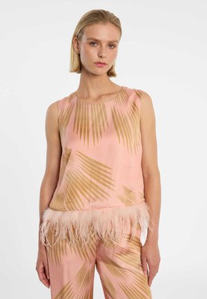 Vrouw draagt een roze mouwloze top en broek met bruine palmbladeren patronen, de zoom van de top is versierd met zachte roze veren.