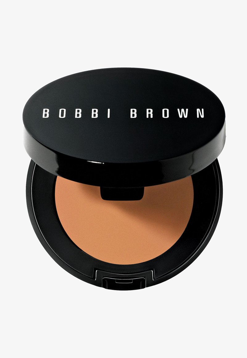 Compatto di trucco nero con una polvere beige liscia all'interno. La parte superiore presenta il logo bianco "BOBBI BROWN". Il compatto ha una forma rotonda e una finitura lucida.