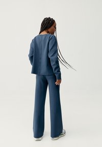 Tmavo modrý, hladký teplákový súprava s voľným strihom, ktorý má spustené ramená a široké nohavice, doplnené minimalistickým detailom zadného švu.