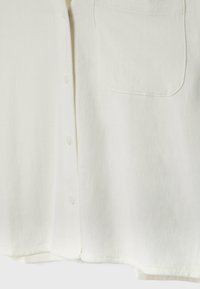 Camicia bianca con bottoni, realizzata in un tessuto texture, dotata di una singola tasca sul petto e sei leggeri bottoni lungo il davanti.