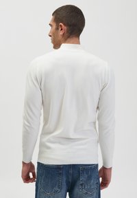 Maglione bianco a maniche lunghe con colletto rotondo, texture lavorata a maglia e polsini a costine, abbinato a jeans in denim blu sbiaditi.