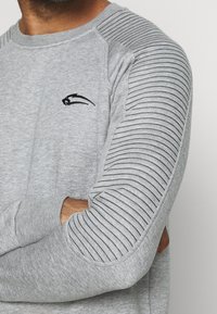 Felpa grigia con maniche a righe a costine, collo rotondo e piccolo logo ricamato sul petto. Tessuto morbido, vestibilità comoda.