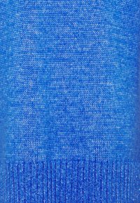 Nära bild av blått stickat tyg som visar detaljerad sömmönster och textur.