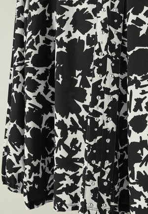 Tessuto a fantasia in bianco e nero con forme astratte, caratterizzato da paillettes decorative lungo la chiusura e dettagli arricciati all'orlo.