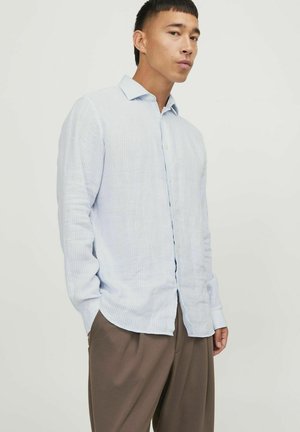 Chemise à rayures bleu clair à manches longues avec un col boutonné, en tissu doux et avec une coupe décontractée. Associée à un pantalon ample marron.