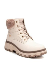 Botas de tobillo beige con cuello de pelo sintético, diseño con cordones, herrajes dorados y suela de goma gruesa con un patrón de relieve.