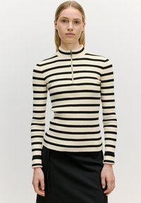 Schwarz-weißer gestreifter Rippstrick-Top mit hohem Kragen und kurzem Reißverschluss. Lange Ärmel, figurnaher Schnitt, betonte Textur.