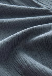 Dunkelblauer, strukturierter Stoff mit weichem Fall, der dezente Rillenmuster und eine matte Oberfläche aufweist. Glatte Oberfläche mit Lichtspiel.