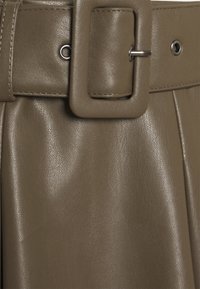 Gros plan sur une ceinture en simili cuir marron avec une boucle carrée et une surface texturée, cintrant un vêtement plissé.