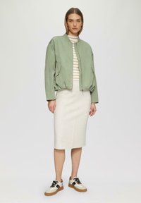 Giacca bomber verde chiaro, maglietta a righe, gonna a matita beige e sneaker multicolore. Tessuto morbido con un taglio moderno e due tasche frontali.