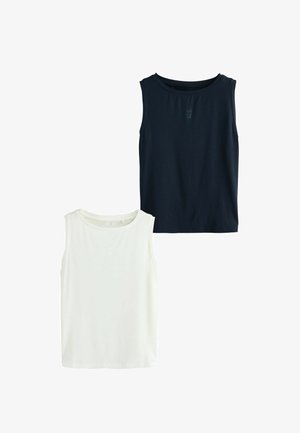 Frau mit lockigem Haar, die ein ärmelloses marineblaues Oberteil und schwarze Shorts trägt, vor einem schlichten weißen Hintergrund steht und nach unten schaut, dabei die Hand in der Nähe des Ohrs hält.