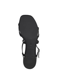 Musta sandaali, jossa on teksturoitu pohja, säädettävät remmit ja litteä kantapää. Suunnittelussa on sileä pinta ja vähäisesti metalliosia.
