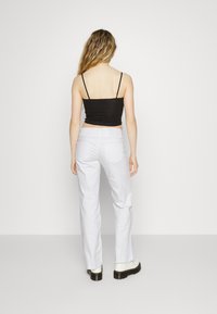 Top de alças ajustado preto e jeans brancos de cintura alta com pernas retas. Botas brancas até o tornozelo com solas grossas e detalhes em preto.