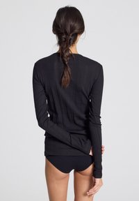 Maglietta nera a maniche lunghe con texture a coste. Il design presenta una silhouette aderente con un collo rotondo. Indossata con slip neri.