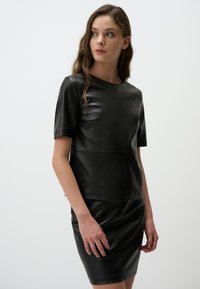 Top in pelle nera con maniche corte e scollatura tonda, caratterizzato da un design aderente e dettagli di cucitura in evidenza, abbinato a una gonna coordinata.