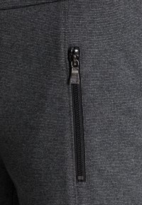 Grijze gestructureerde stof met een ritszak; de rits heeft een slanke trekstrook en zwarte rand langs de opening voor gemakkelijke toegang.