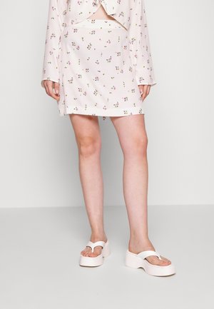 Robe légère rose pâle à motif floral avec un design enveloppant et des manches longues. Associée à des sandales plate-formes blanches avec un design de lanière en forme de V.