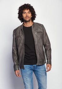 Grau lederne Jacke mit schmaler Passform, mit Reißverschlusstaschen und glatter Textur. Getragen über einem schwarzen Hemd und kombiniert mit blauen Jeans.