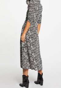 Černobíle vzorované šaty střední délky s nabíranými rukávy, staženým pasem a lehkým materiálem, doplněné černými kotníkovými botami.