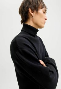 Maglione nero a collo alto realizzato in materiale a maglia testurizzata. Caratterizzato da un alto collo e spalle scese. Design semplice e minimalista.