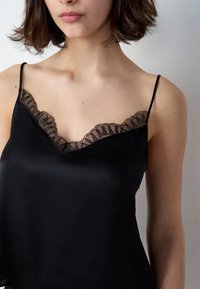 Camisón de satén negro con un escote en V profundo adornado con borde de encaje negro y tirantes delgados ajustables. Textura suave y ajuste relajado.
