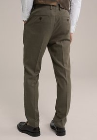 Vékony fazonú oliva színű nadrág texturált anyagból, két hátsó zsebbel gombbal záródik, elöl pedig hajtott. 