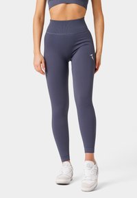 Vysoké elastické legíny v tmavě šedé barvě s přiléhavým střihem. Obsahují malou logo aplikaci a jsou doplněny bílými sportovními botami.