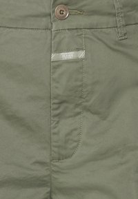 Pantalones de color verde oliva con una textura suave, que presentan un botón marrón, un bolsillo lateral y una pequeña etiqueta "CLOSED" en la cinturilla.