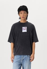 Sort oversized bomulds t-shirt med et grafisk print i midten, der skildrer en byscene, korte ærmer og rund halsudskæring.