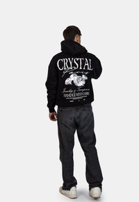 Czarny hoodie z dużym białym napisem i grafiką diamentu na plecach, w połączeniu z ciemnoszarymi dżinsami i białymi trampkami.