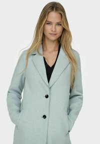 Cappotto in lana azzurro chiaro con rever a punta, dotato di due bottoni neri, tasche laterali e vestibilità rilassata. Superficie testurizzata visibile.