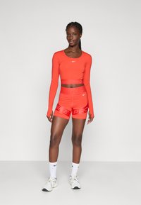 Red long-sleeve crop top and matching high-waisted shorts with a "NIKE PRO" waistband. Finished with white sports socks and athletic shoes.