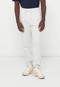 Jasnoszare spodnie dresowe z elastycznym pasem i sznurkiem. Gładka tekstura, zwężane nogawki, w połączeniu z beżowymi butami sportowymi.