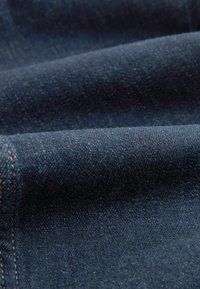 Gros plan d’un tissu en denim bleu foncé montrant la texture, le tissage et les détails de couture sur un matériau plié.