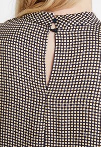 Mörkblå och krämfärgad mönstrad blus med en nyckelhålsdesign på baksidan, två svarta knappstängningar och en strukturerad tygfinish.