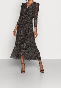 Schwarzes Kleid mit V-Ausschnitt, langen durchsichtigen Ärmeln und einem rüschierten, knielangen Saum. Es hat ein geometrisches Muster in Beige und Braun.
