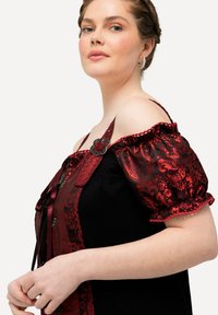 Top scollato con base nera, maniche a sbuffo con motivo rosso, fibbia decorativa e dettagli in pizzo lungo la parte anteriore e le maniche.