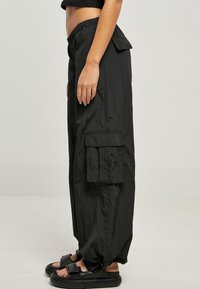 Czarne spodnie cargo wykonane z lekkiego materiału, o luźnym kroju, z bocznymi kieszeniami i elastycznymi mankietami, w połączeniu z czarnymi sandałami.