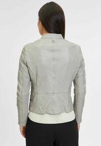 Giubbotto in pelle grigia con un design aderente, cuciture testurizzate e un dettaglio a bottone sul retro. Presenta un orlo bianco a coste.