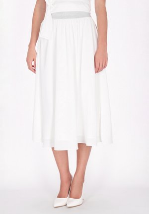 La modelo lleva una falda midi blanca y vaporosa, con cinturilla gris y zapatos de tacón blancos a juego con punta afilada.