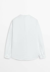 Chemise blanche à manches longues boutonnée vue de dos, avec un ourlet droit et des poignets boutonnés sur un fond blanc uni.