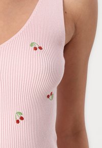 Top in cotone rosa a costine con piccoli ricami di ciliegie rosse. Il tessuto ha un aspetto texturizzato, con un design a scollo a V.