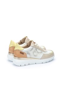 Zapatillas blancas con acentos en beige, amarillo y marrón claro, con un diseño perforado, cordones y una suela blanca gruesa.