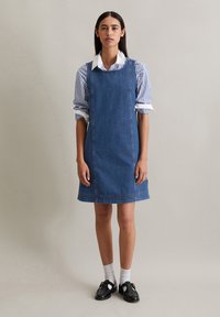 Denim jurk met een losse pasvorm, voorzien van een ronde halslijn en rechte zoom. Gecombineerd met een blauw-witte gestreepte blouse met kraag.