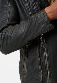 Schwarze Lederbikerjacke mit matter Oberfläche, ausgestattet mit silbernen Reißverschlüssen, strukturiertem Material und verstärkten Nähten entlang der Säume.