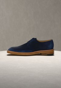 Ανδρικό παπούτσι φόρμας από σουέντ σε ναυτικό μπλε με ελαφριά καφέ ξύλινη σόλα και μαύρο τακούνι, παρουσιάζεται σε ουδέτερη επιφάνεια.