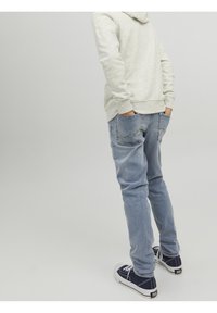 Světle šedá mikina, modré džíny a tmavě modré tenisky. Džíny mají klasický střih, boční kapsy a vybledlý vzhled.