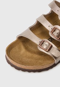 Metalické sandály v odstínu růžového zlata s dvěma širokými pásky, dekorované bronzovými přezkami, semišovou stélkou a strukturální podrážkou.