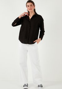 Black button-up shirt with long sleeves, made of lightweight material, paired with white wide-leg pants and black-and-white sneakers.